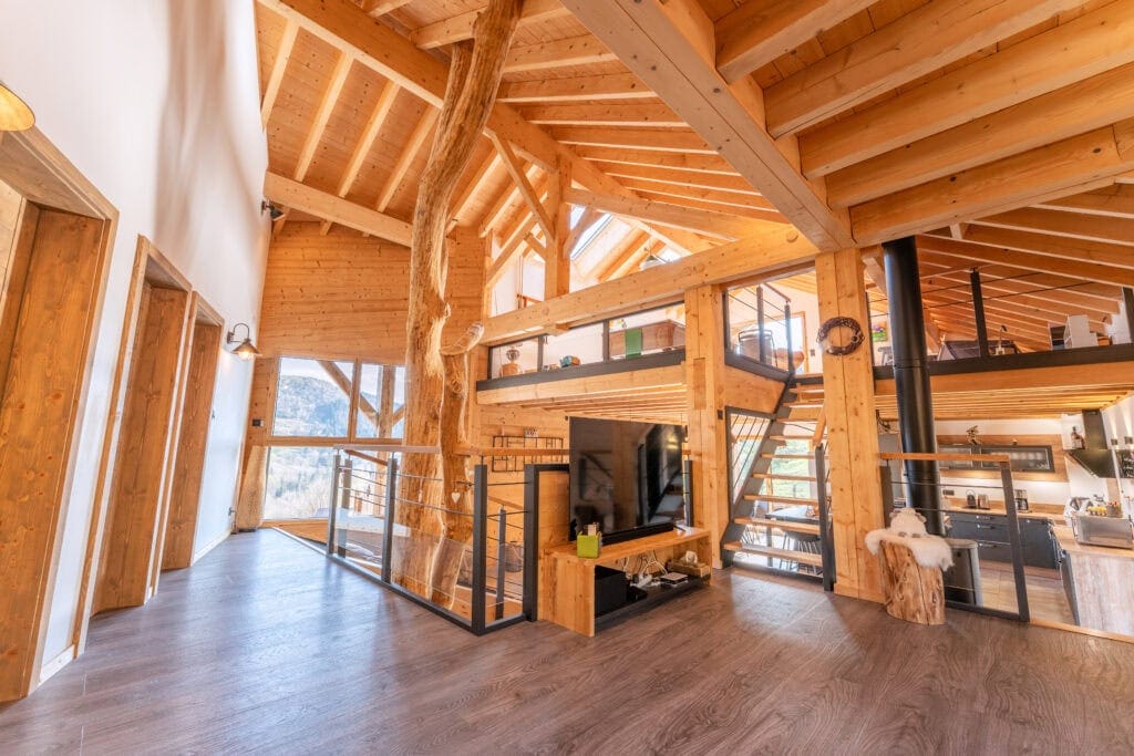 Vaste intérieur en bois d'un chalet à La Bresse, avec poutres apparentes et mezzanine lumineuse.