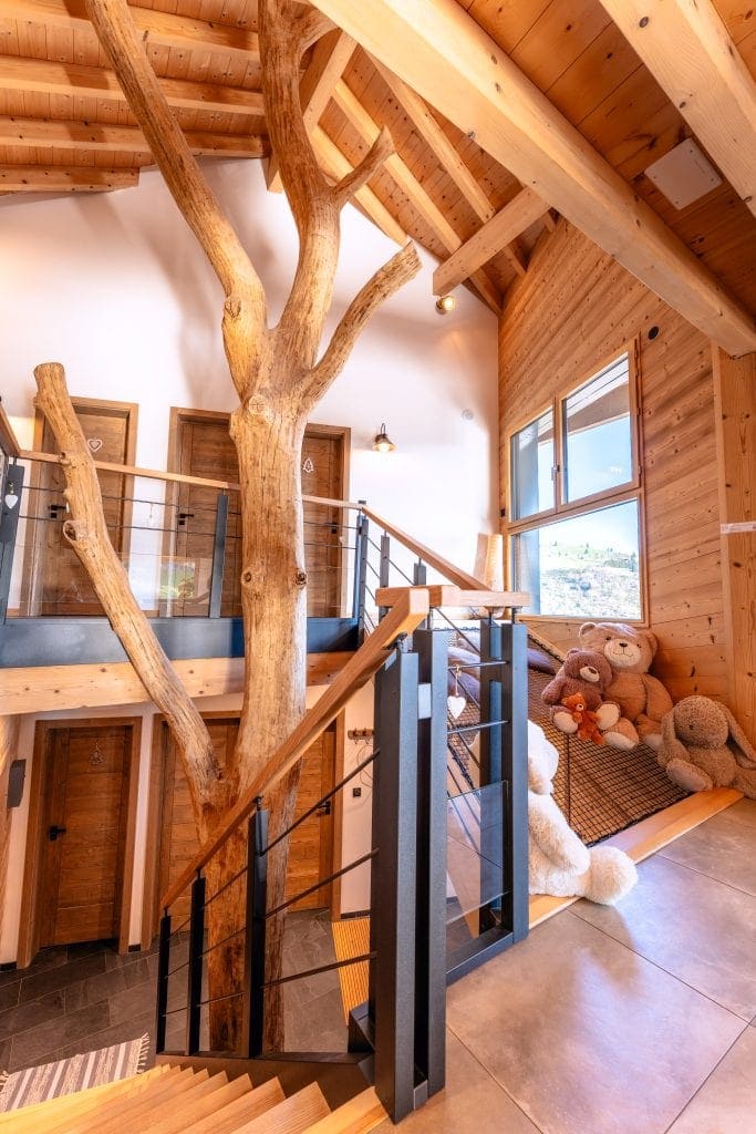 Échelle intérieure en bois avec arbre décoratif niche à teddy bears, luminosité naturelle, style chalet moderne.